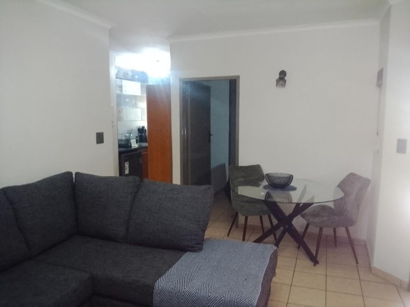 Open plan living and dining area with tiled flooring, leading to a kitchen and additional room access.