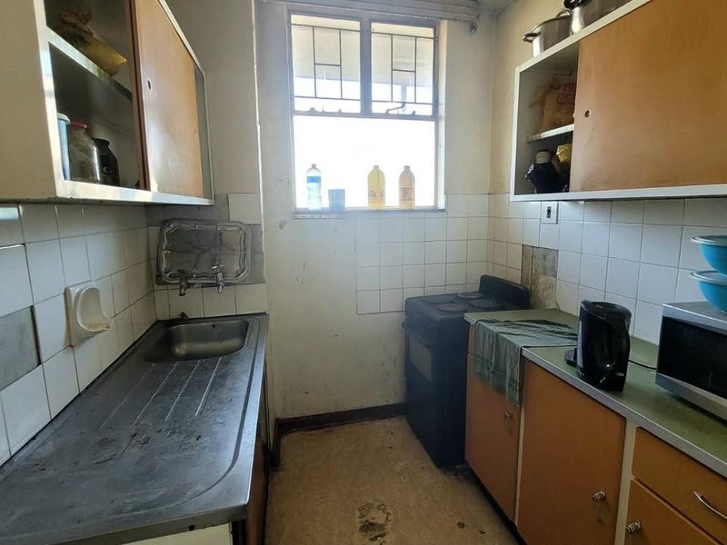 A compact, dated kitchen featuring original cabinetry, a stainless steel sink, and a tiled backsplash, requiring significant renovation and modernization.