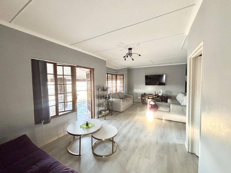 Spacious living room featuring light-toned laminate flooring, neutral grey walls, and direct access to an outdoor patio area through wooden french doors.