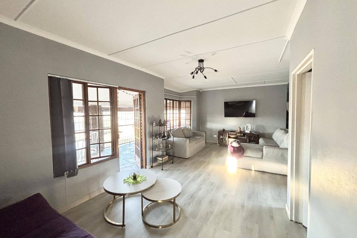 Spacious living room featuring light-toned laminate flooring, neutral grey walls, and direct access to an outdoor patio area through wooden french doors.