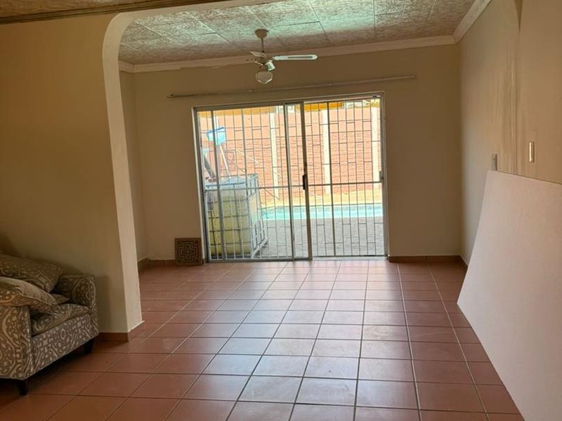 Spacious living area featuring tiled flooring, decorative pressed metal ceilings, and sliding glass doors providing direct access to the outdoor pool area.