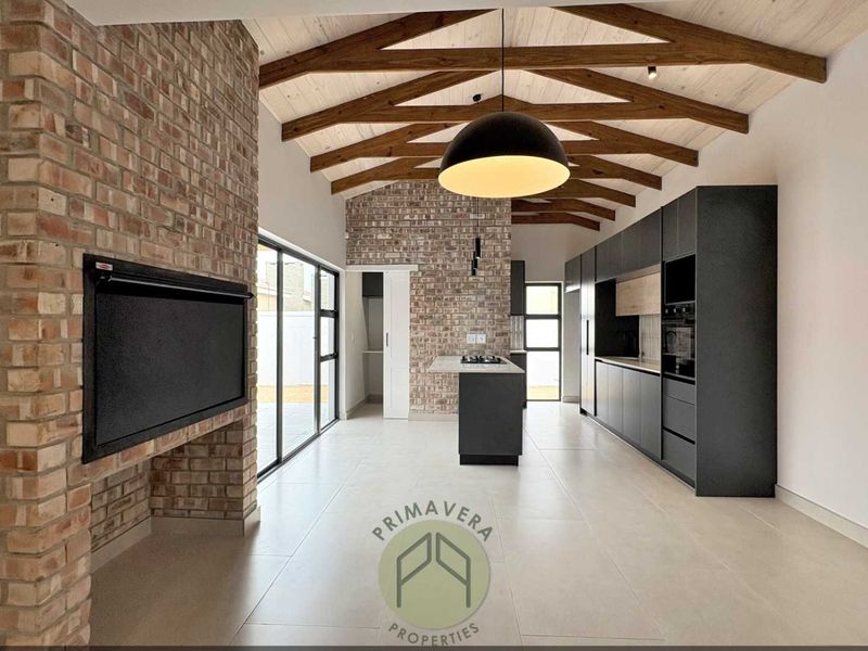 Modern open-plan living and kitchen area featuring exposed brickwork, timber vaulted ceilings, a central island, and sleek built-in cabinetry with integrated appliances.