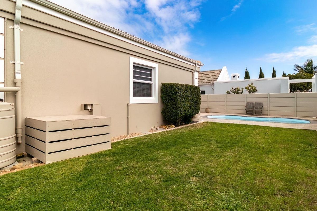 A well-maintained rear garden featuring a swimming pool, lawn area, and a rainwater collection tank attached to the side of the house.