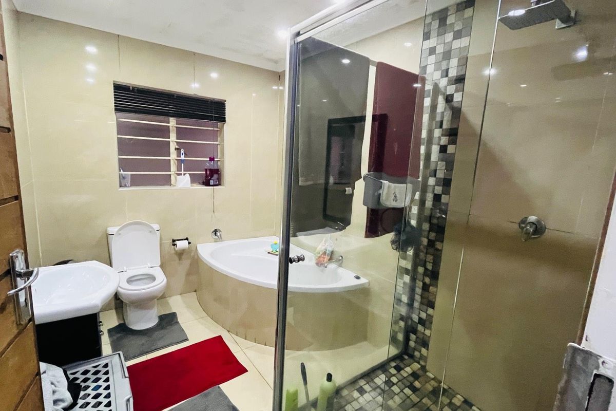 A functional bathroom featuring a corner bathtub, a separate glass-enclosed shower with mosaic tile accents, a pedestal basin, and a toilet.