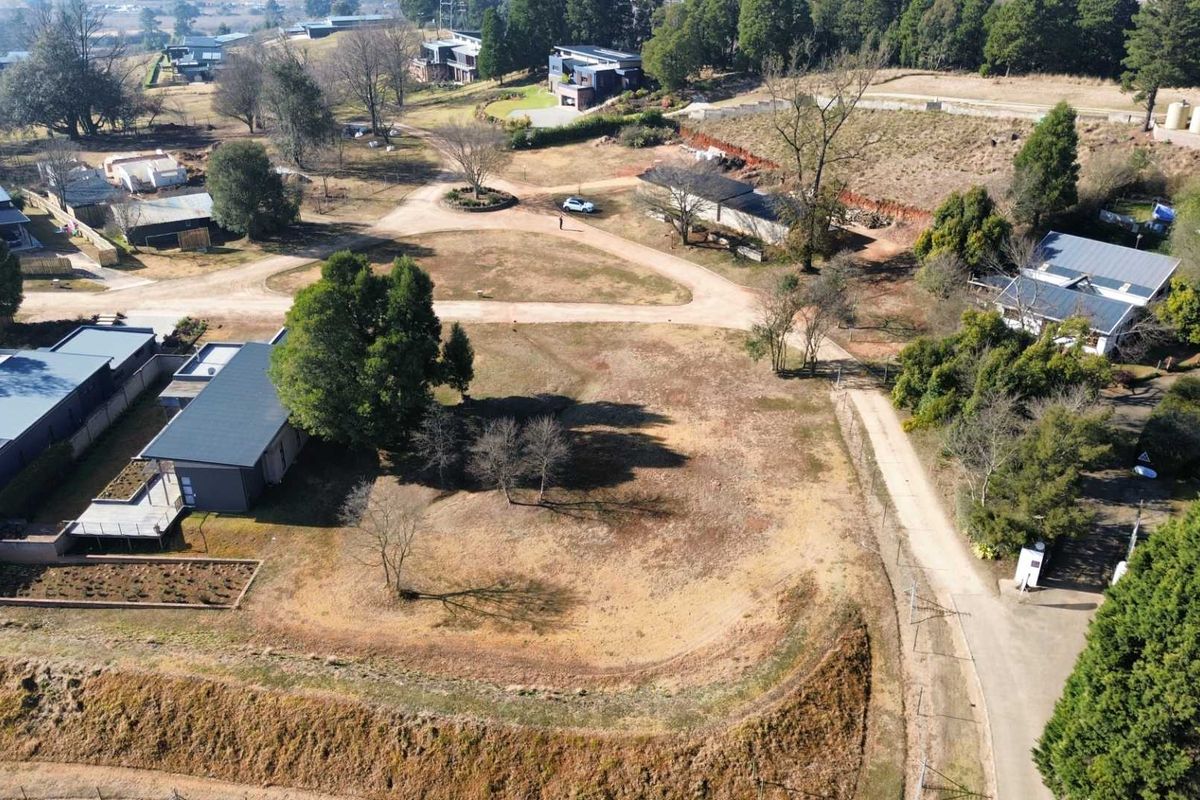 Aerial view of a vacant residential plot featuring natural terrain, mature trees, and access via a gravel road within a developed estate setting.