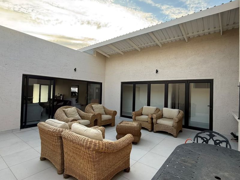 A spacious covered patio featuring large sliding glass doors, tiled flooring, and a built-in fireplace, perfect for outdoor entertaining.