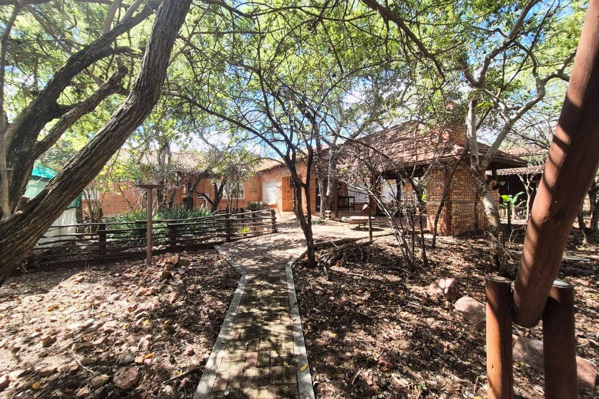 A view of the rear exterior of the house featuring a brick facade, a paved walkway, and a mature garden setting.