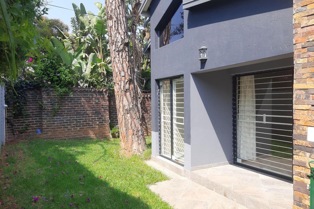 Rear view of the cottage featuring a paved patio area, sliding glass doors with security gates, and a private garden with brick boundary wall.