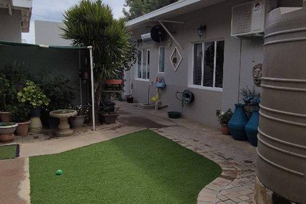 A rear garden area featuring artificial turf, paved walkways, and a large water storage tank attached to the side of the house.