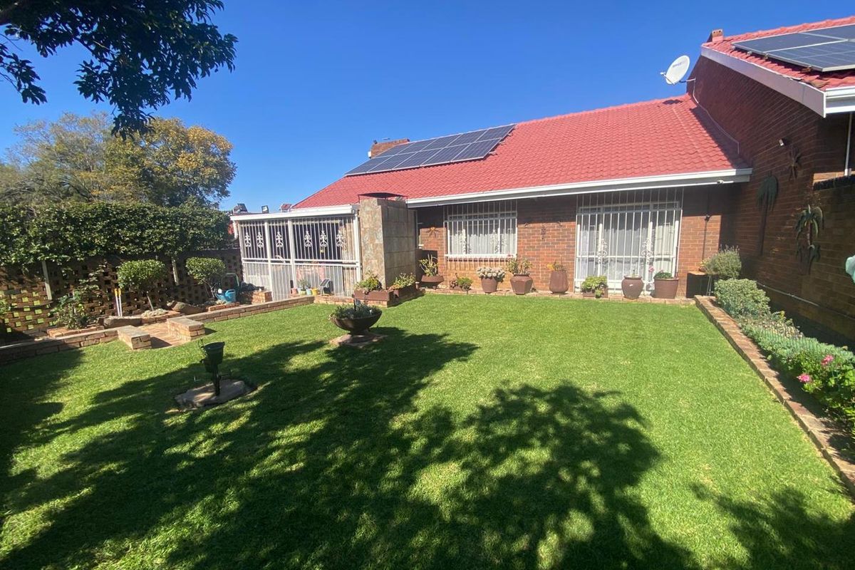 A well-maintained rear garden featuring a manicured lawn, brick boundary walls, and a townhouse exterior with solar panels and security bars on windows.