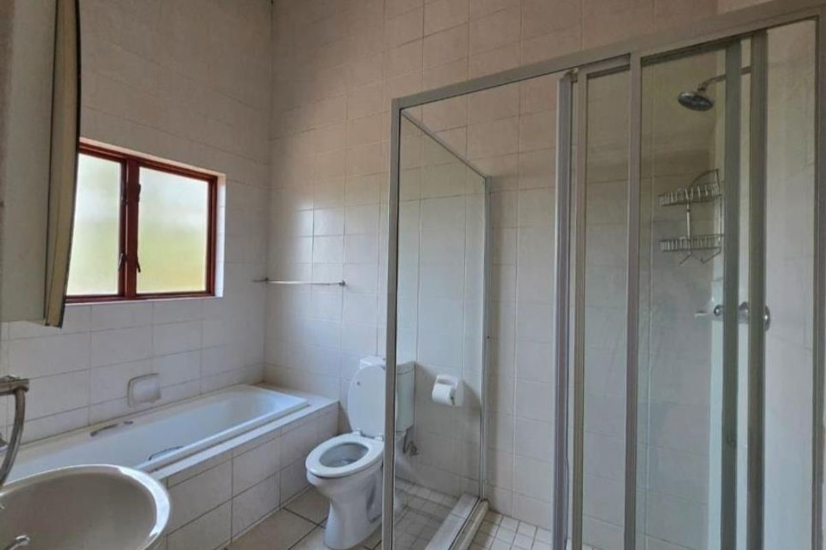 A functional bathroom featuring a built-in bathtub, separate glass-enclosed shower, toilet, and pedestal basin with tiled walls and flooring.