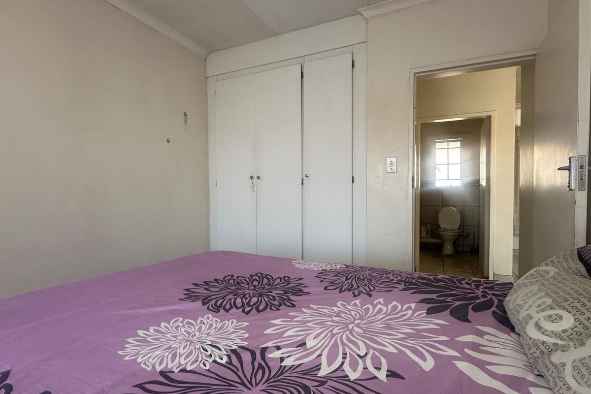 A bedroom featuring built-in cupboards and an en-suite bathroom with tiled flooring and natural light.