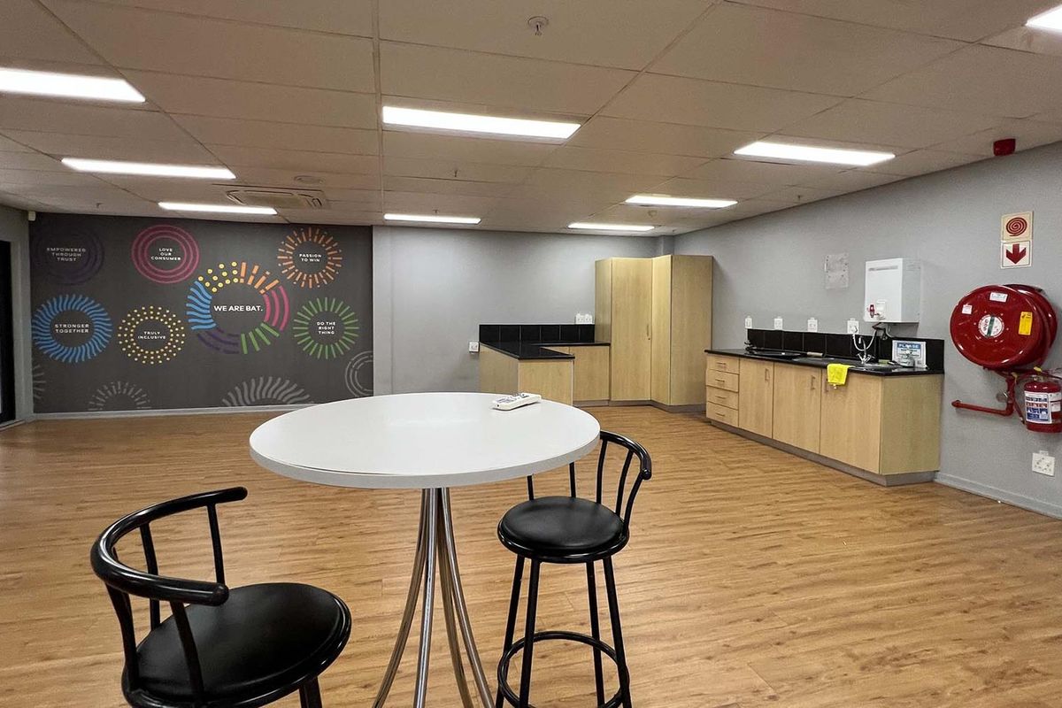 A functional industrial breakroom featuring a kitchenette with built-in cabinetry, laminate flooring, suspended ceiling, and essential fire safety equipment.