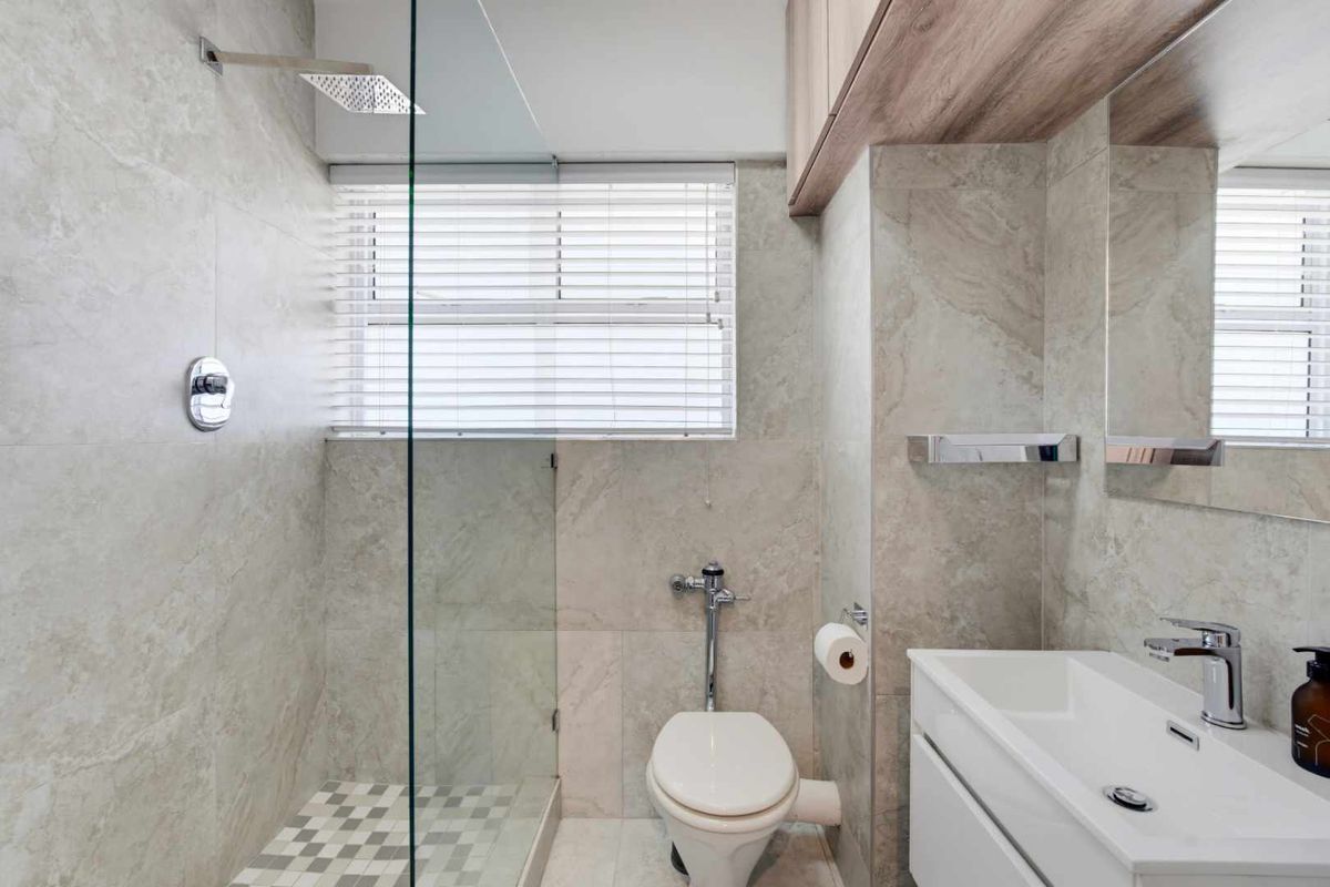 Modern bathroom featuring a walk-in shower with a rain shower head, wall-mounted toilet, vanity with basin, and neutral stone-look tiling throughout.