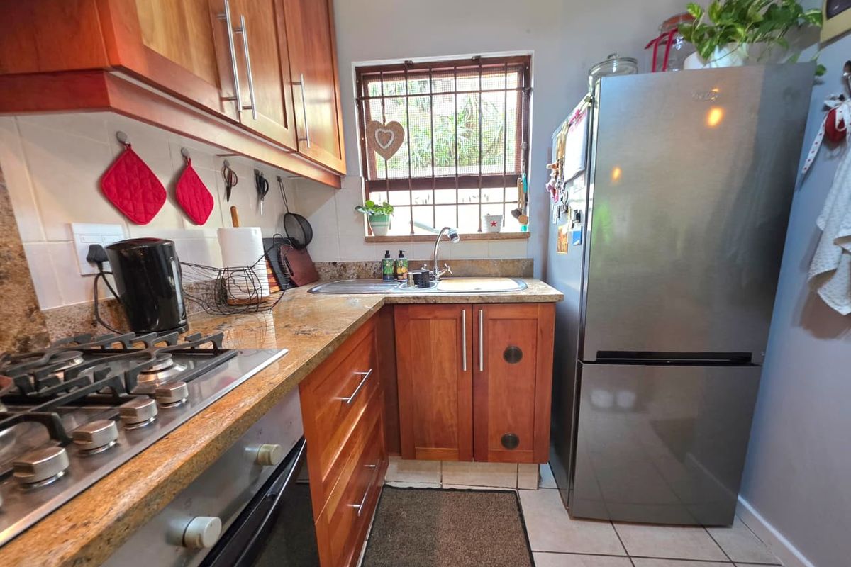 Compact kitchen featuring wooden cabinetry, granite countertops, a built-in gas hob, oven, and a stainless steel sink with security bars on the window.