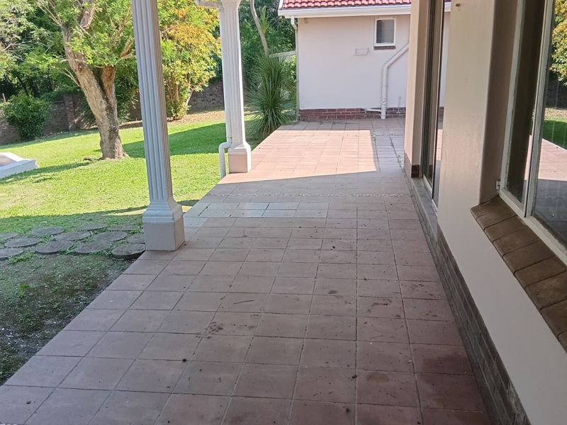 A covered outdoor patio area featuring tiled flooring, decorative columns, and direct access to the garden through sliding glass doors.