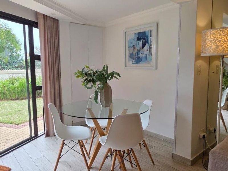Bright open-plan living and dining area featuring tiled flooring, a mirrored wall feature, and large sliding glass doors opening to a private garden.