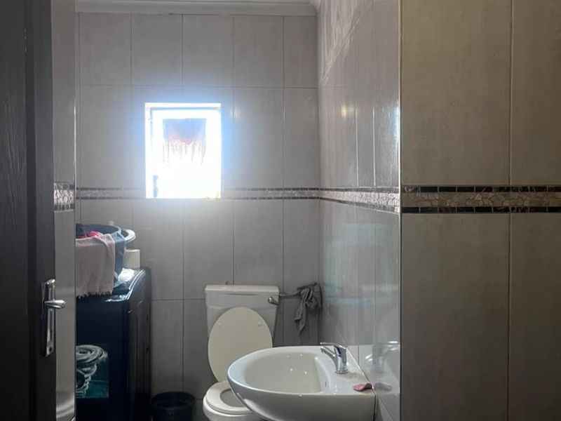 A functional bathroom featuring a pedestal basin, toilet, and neutral ceramic wall and floor tiling with a small window for natural light.