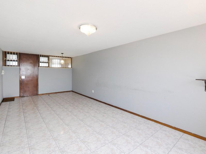 An empty, open-plan living area featuring neutral tiled flooring, a secure entrance door, and simple wall finishes, ready for personalization.
