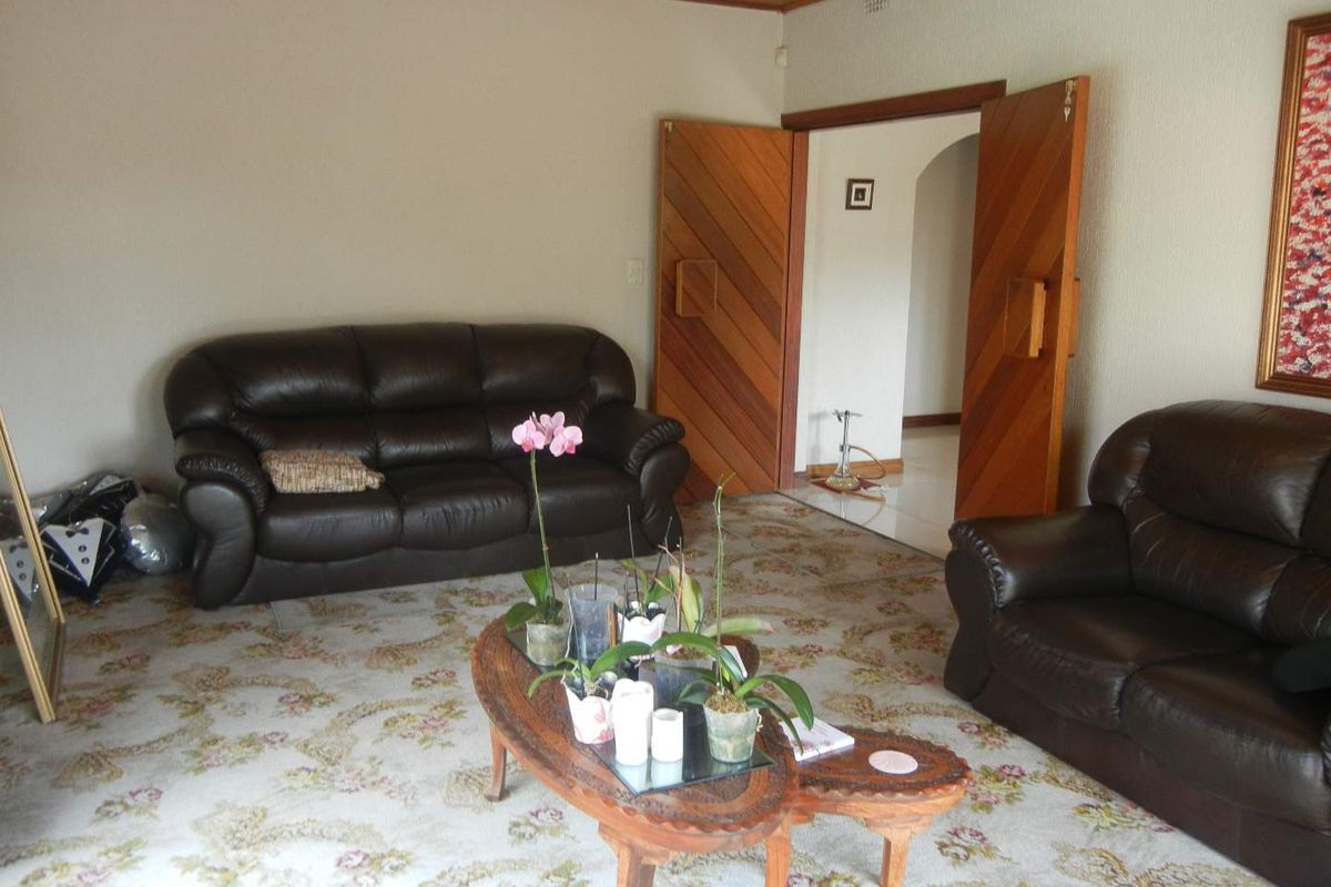 A living room featuring patterned wall-to-wall carpeting, a timber-paneled ceiling, and double wooden doors leading to an adjacent hallway.
