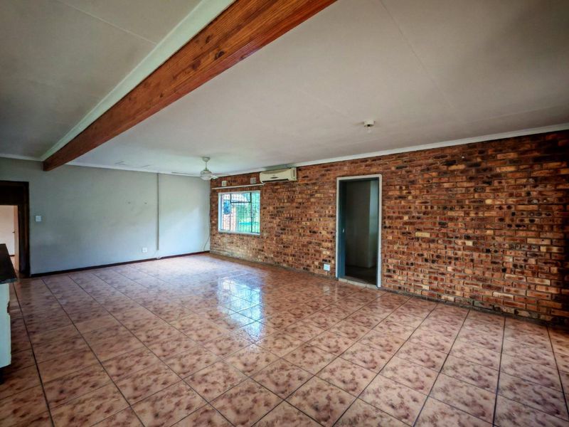 Spacious living area featuring an exposed brick feature wall, timber ceiling beam, ceramic tiled flooring, and a wall-mounted air conditioning unit.