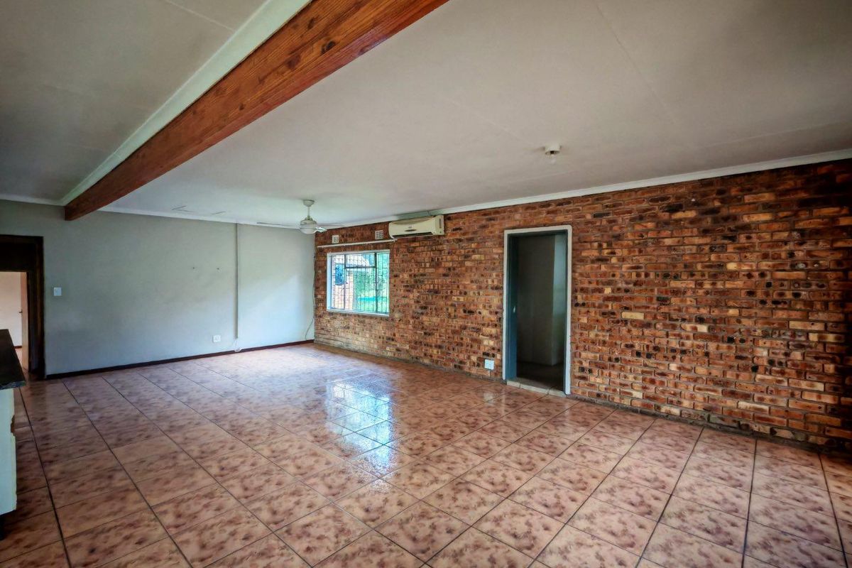 Spacious living area featuring an exposed brick feature wall, timber ceiling beam, ceramic tiled flooring, and a wall-mounted air conditioning unit.