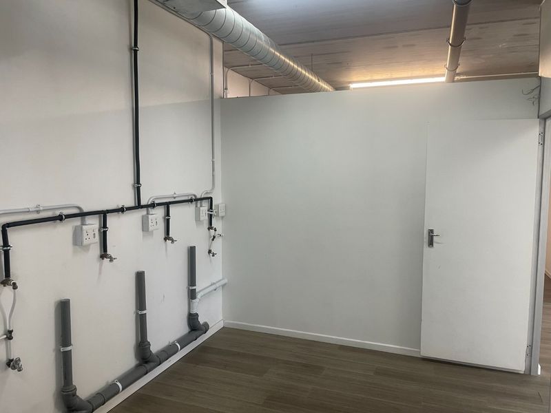 A clean, functional utility space featuring exposed industrial-style plumbing, electrical conduits, and ventilation ducting with durable laminate flooring.