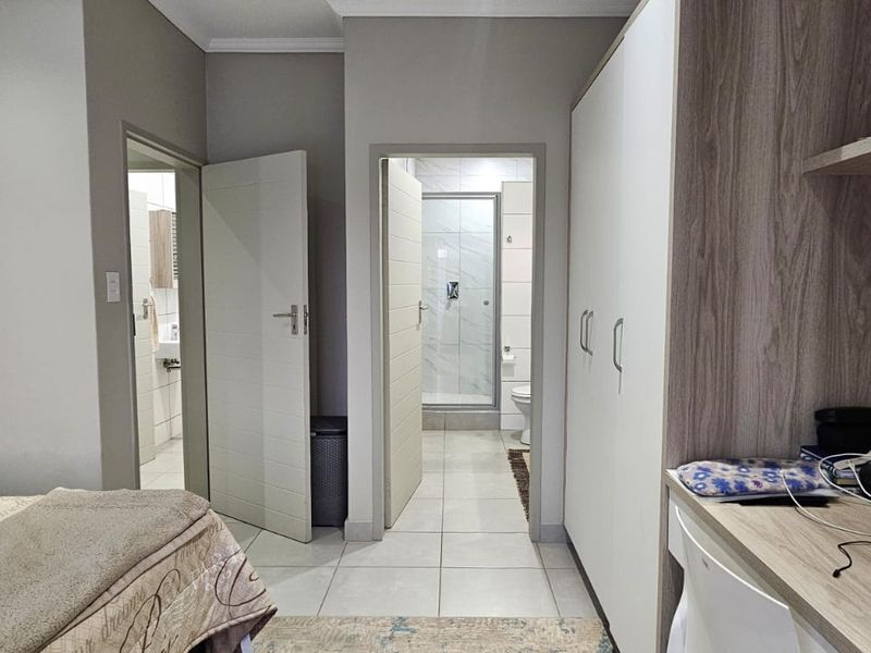A well-maintained bedroom featuring built-in cupboards, a integrated desk area, and direct access to an en-suite bathroom with tiled flooring throughout.