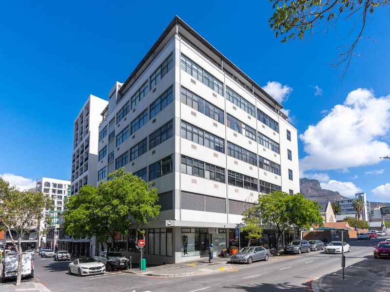 A prominent multi-story corner office building featuring extensive glass windows and ground-level retail space, situated in a vibrant urban street setting.