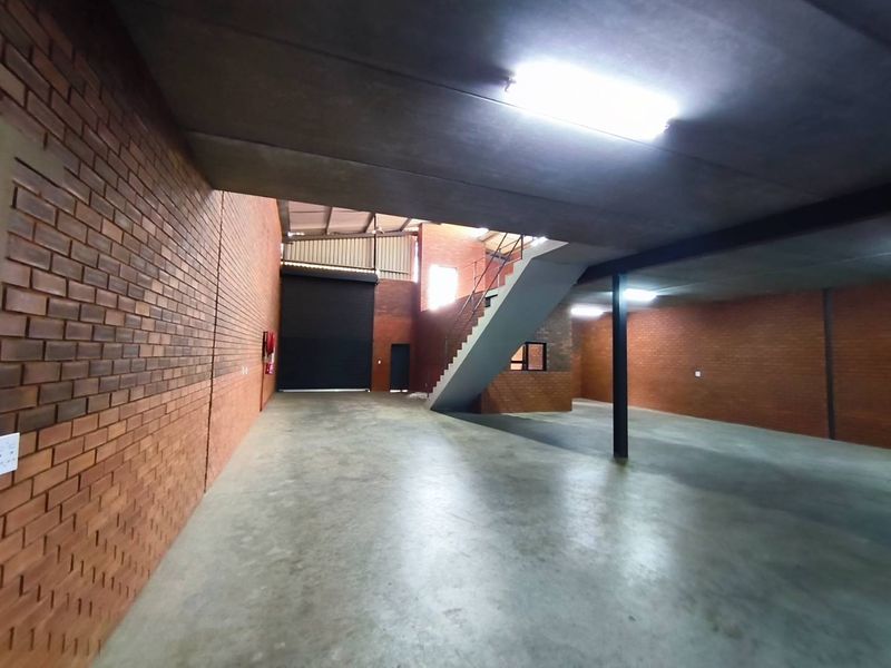 Spacious industrial utility area featuring exposed brick walls, polished concrete flooring, a roller shutter door, and a staircase leading to an upper level.