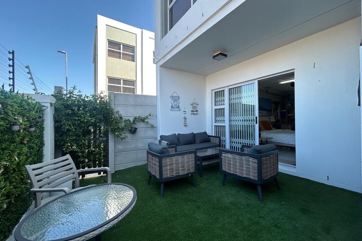A private rear patio area featuring artificial turf, a covered seating space, and direct access to the interior through sliding glass doors.