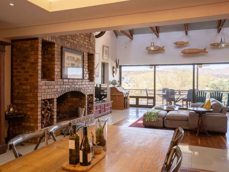 Spacious open-plan living and dining area featuring a prominent brick fireplace, exposed timber beams, and large sliding doors opening to a scenic balcony.