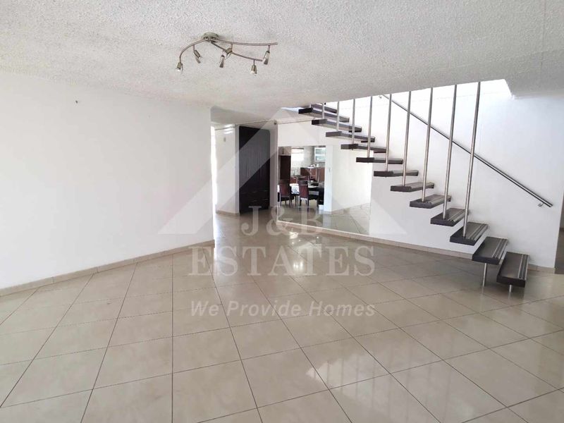 Spacious open-plan living area featuring tiled flooring and a modern floating staircase with a metal handrail.
