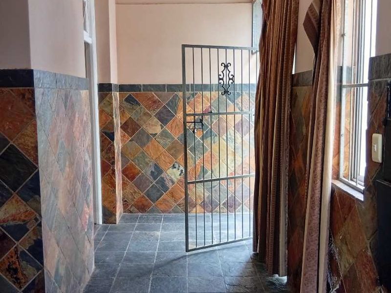 A hallway featuring slate tile flooring and matching slate wall cladding, equipped with a security gate and wall-mounted lighting.
