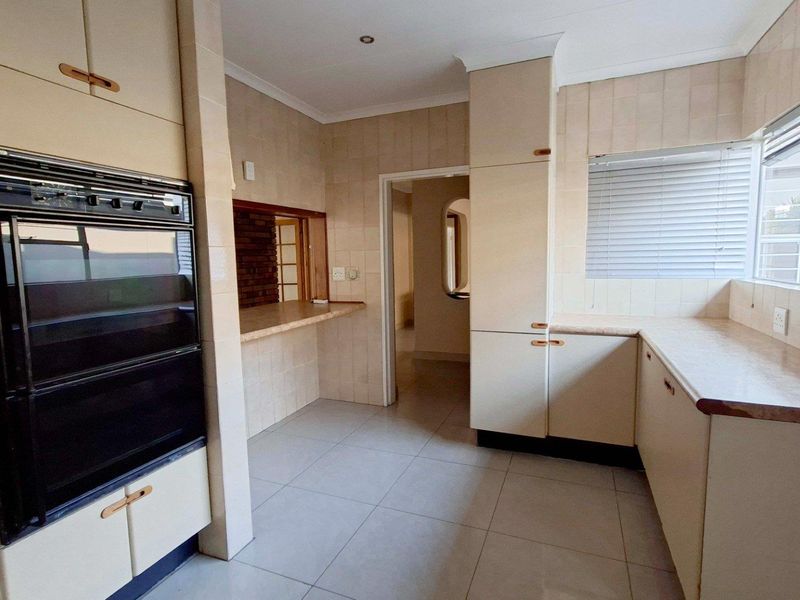 A functional kitchen featuring built-in cabinetry, a wall-mounted oven, tiled splashbacks, and ample counter space, offering a clean canvas for modern updates.