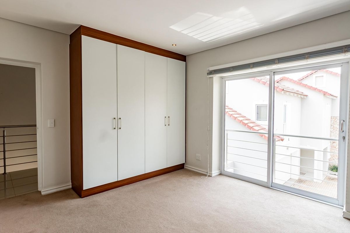 A bright bedroom featuring built-in floor-to-ceiling wardrobes with a wood-trim finish, neutral carpeting, and sliding glass doors leading to a balcony.