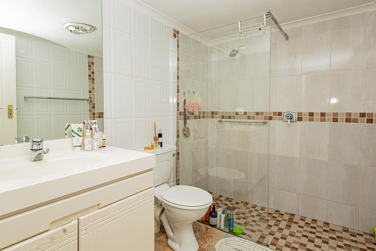 A functional bathroom featuring a vanity with integrated sink, a toilet, and a walk-in shower with a glass screen and tiled finishes.