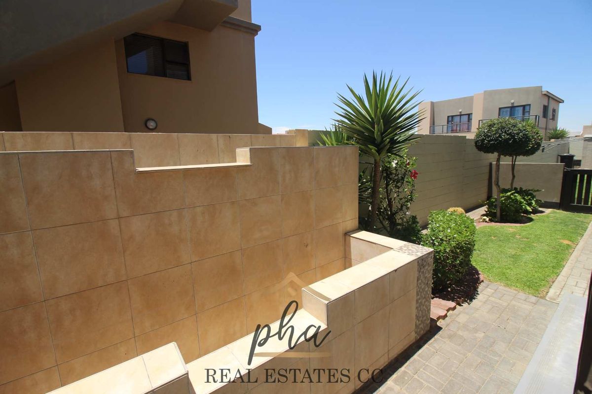 A private rear garden area featuring a tiled feature wall, paved walkway, and a small lawn, providing a low-maintenance outdoor space.
