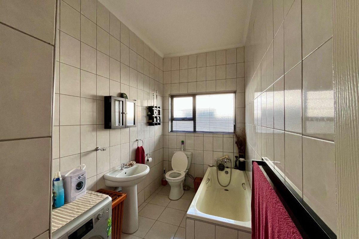 A functional bathroom featuring a pedestal basin, a standard bathtub, and a toilet, with full-height wall tiling and integrated laundry space.