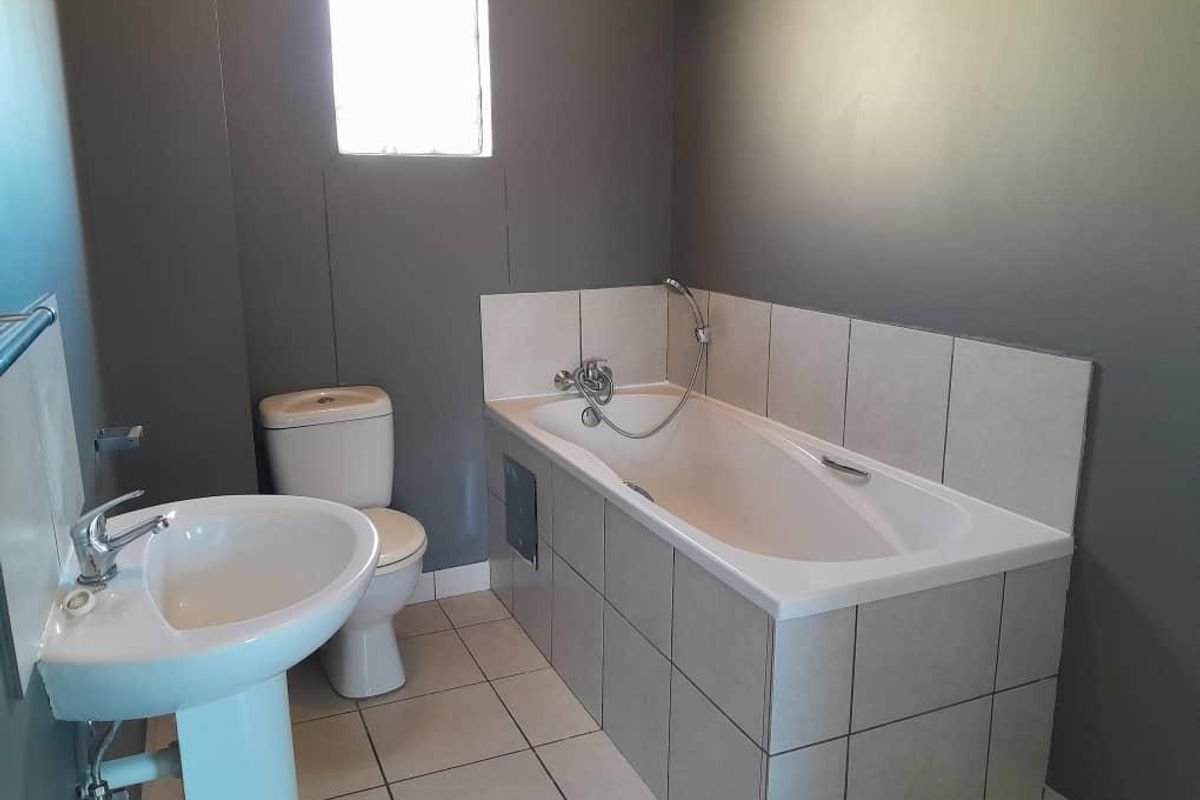 A functional bathroom featuring a pedestal washbasin, toilet, and a tiled bathtub with a shower mixer.