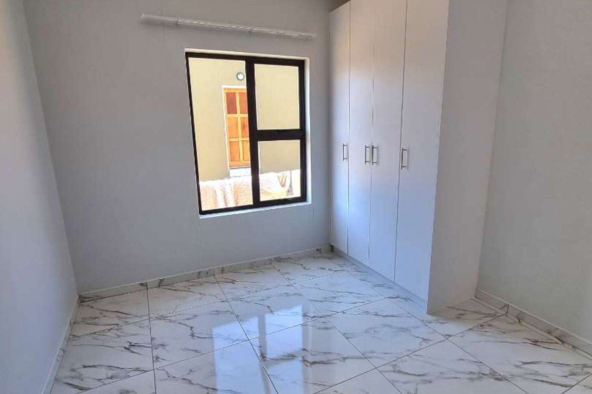 A bright, modern bedroom featuring large-format marble-look floor tiles and a built-in white wardrobe with clean lines.