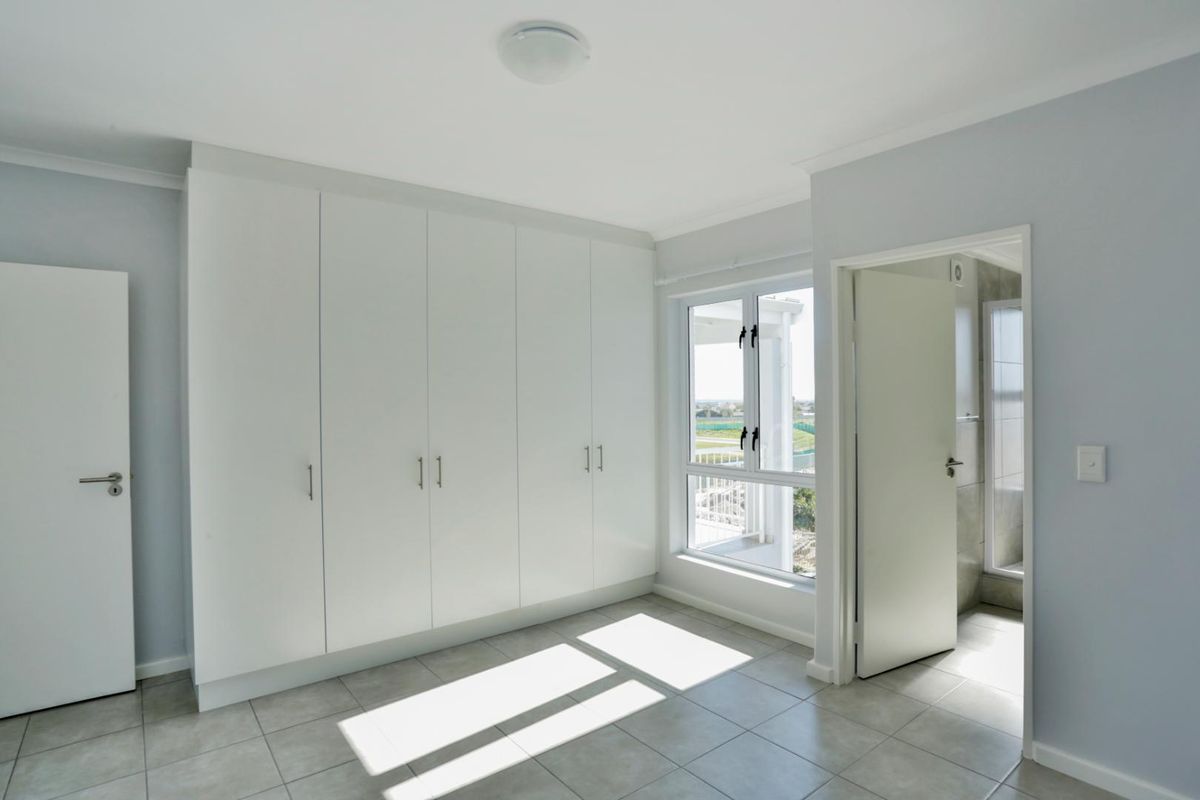A bright, empty bedroom featuring built-in floor-to-ceiling wardrobes, tiled flooring, and an en-suite bathroom entrance.