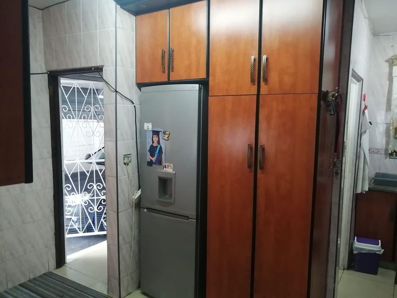 A kitchen area featuring built-in wooden cabinetry and tiled wall finishes, with an adjacent doorway leading to an exterior security gate.