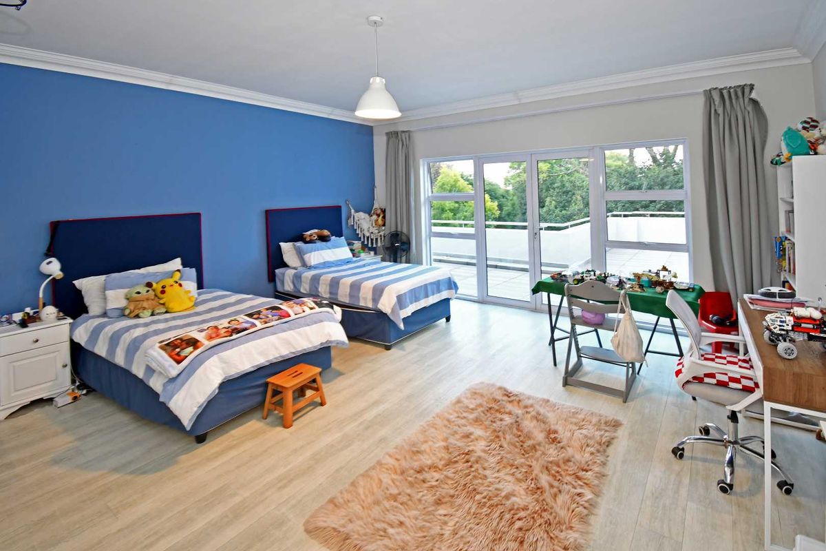 Spacious bedroom featuring light wood-look flooring, a vibrant blue accent wall, and large glass sliding doors opening onto a private balcony.