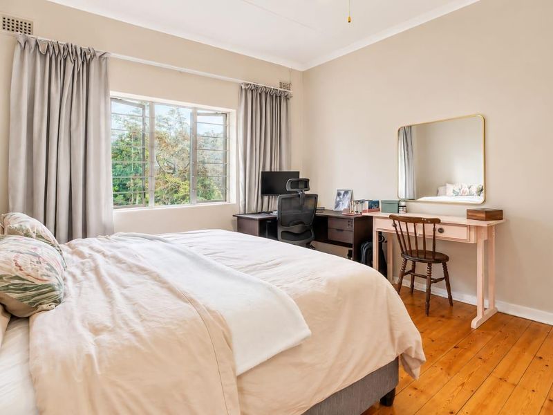 A well-lit bedroom featuring polished timber flooring, neutral wall tones, and large casement windows providing natural light and garden views.