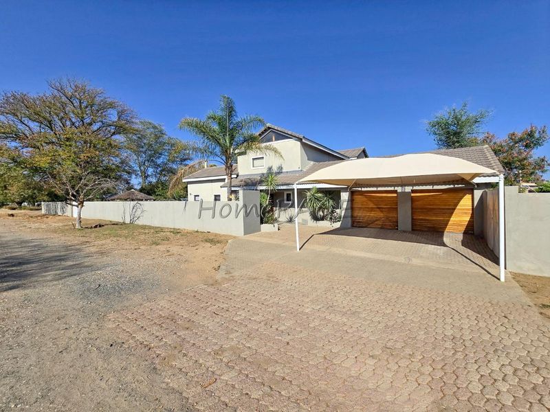 Front exterior view of the property featuring a paved driveway, double garage with wooden doors, and a shade cloth carport.
