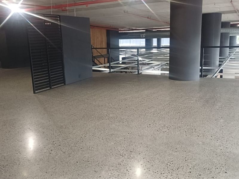 Spacious open-plan retail or commercial mezzanine level featuring polished concrete floors, exposed industrial ceilings, and modern glass balustrades.