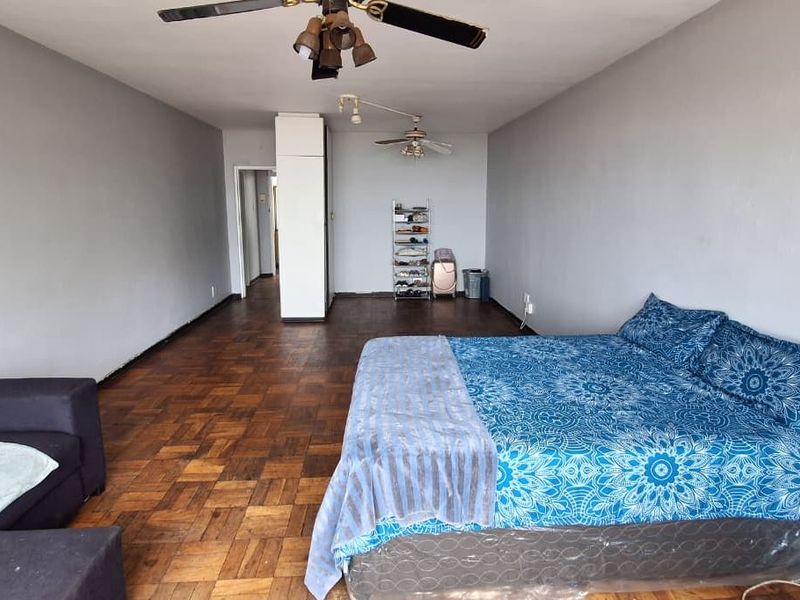 Spacious bedroom featuring classic parquet flooring, dual ceiling fans, and a built-in cupboard, offering a functional layout with neutral wall finishes.