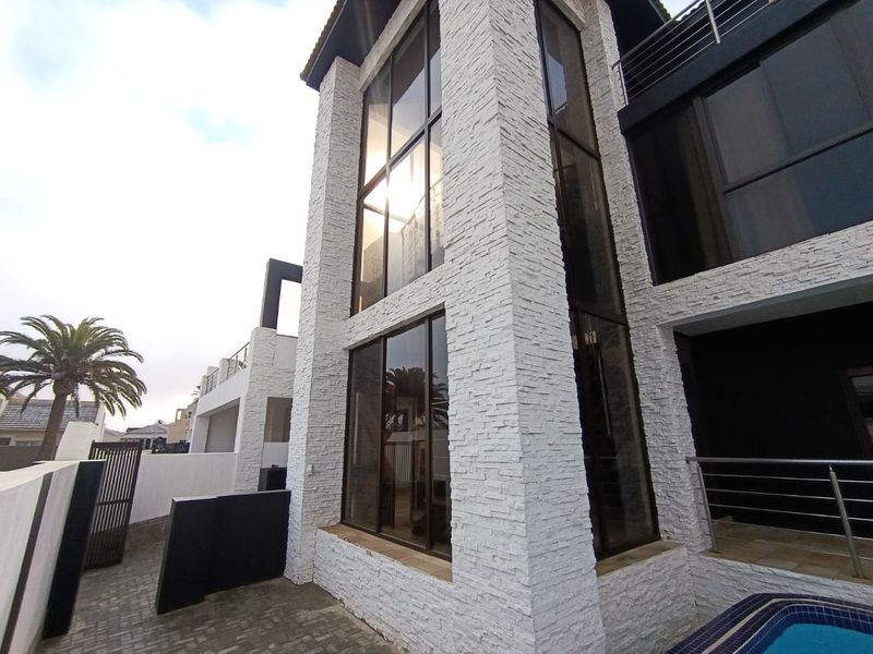 Modern rear exterior view featuring stacked stone facade, expansive glass windows, a swimming pool, and paved patio area.