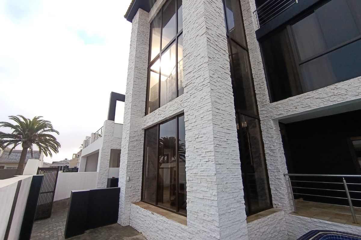 Modern rear exterior view featuring stacked stone facade, expansive glass windows, a swimming pool, and paved patio area.